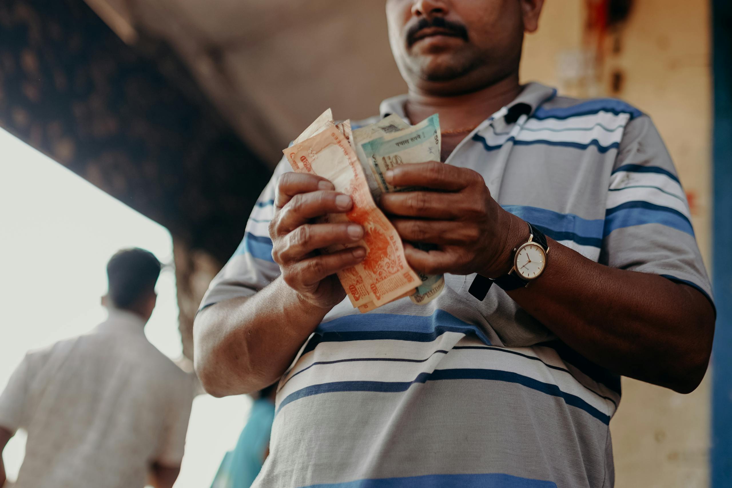 Man in Indian market counting rupee notes, showcasing daily street commerce.