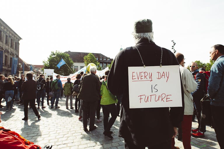 Participants at a climate rally gather on a cobblestone street with signs advocating for the future.