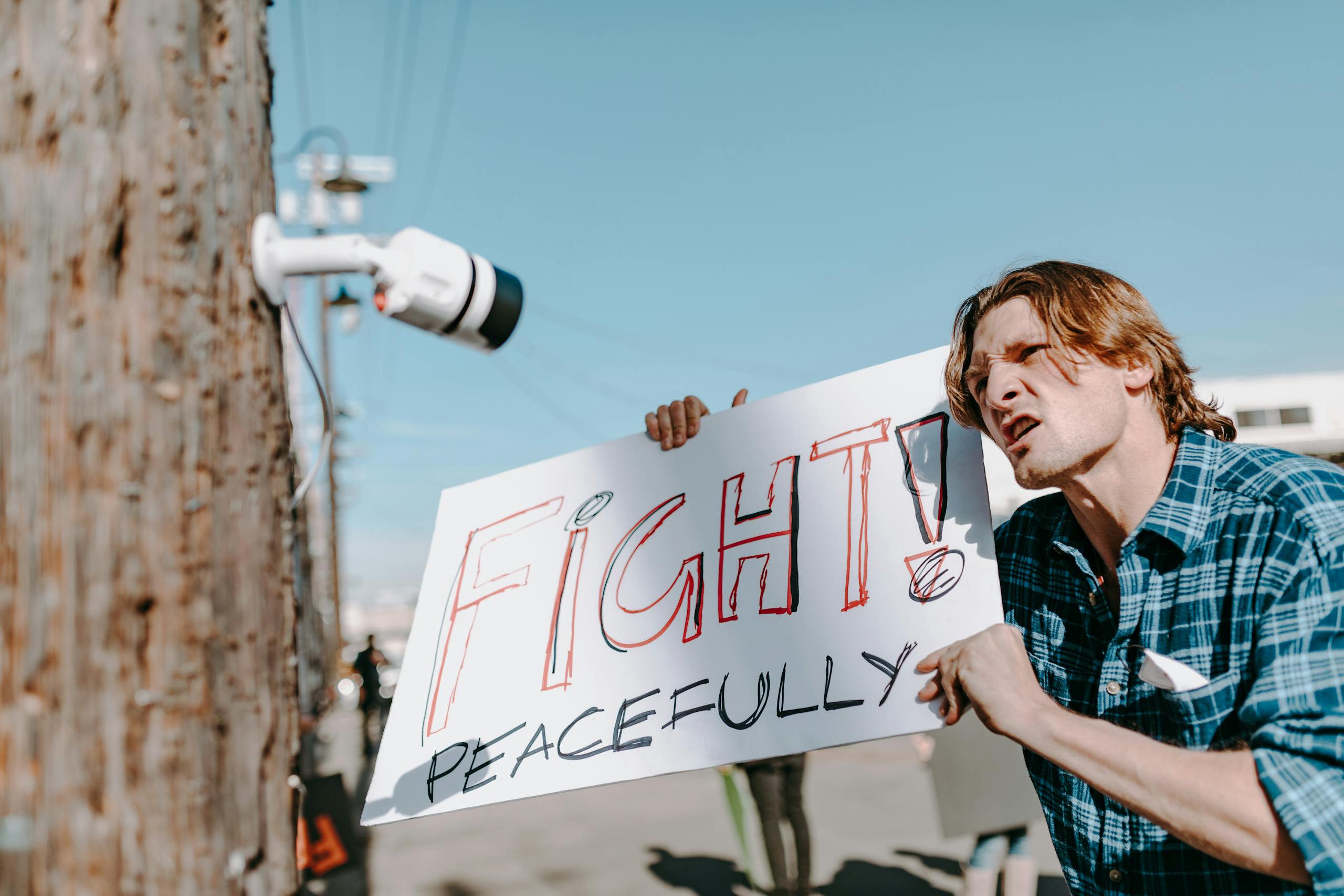 Protester holding a sign for peaceful protest near surveillance camera.
